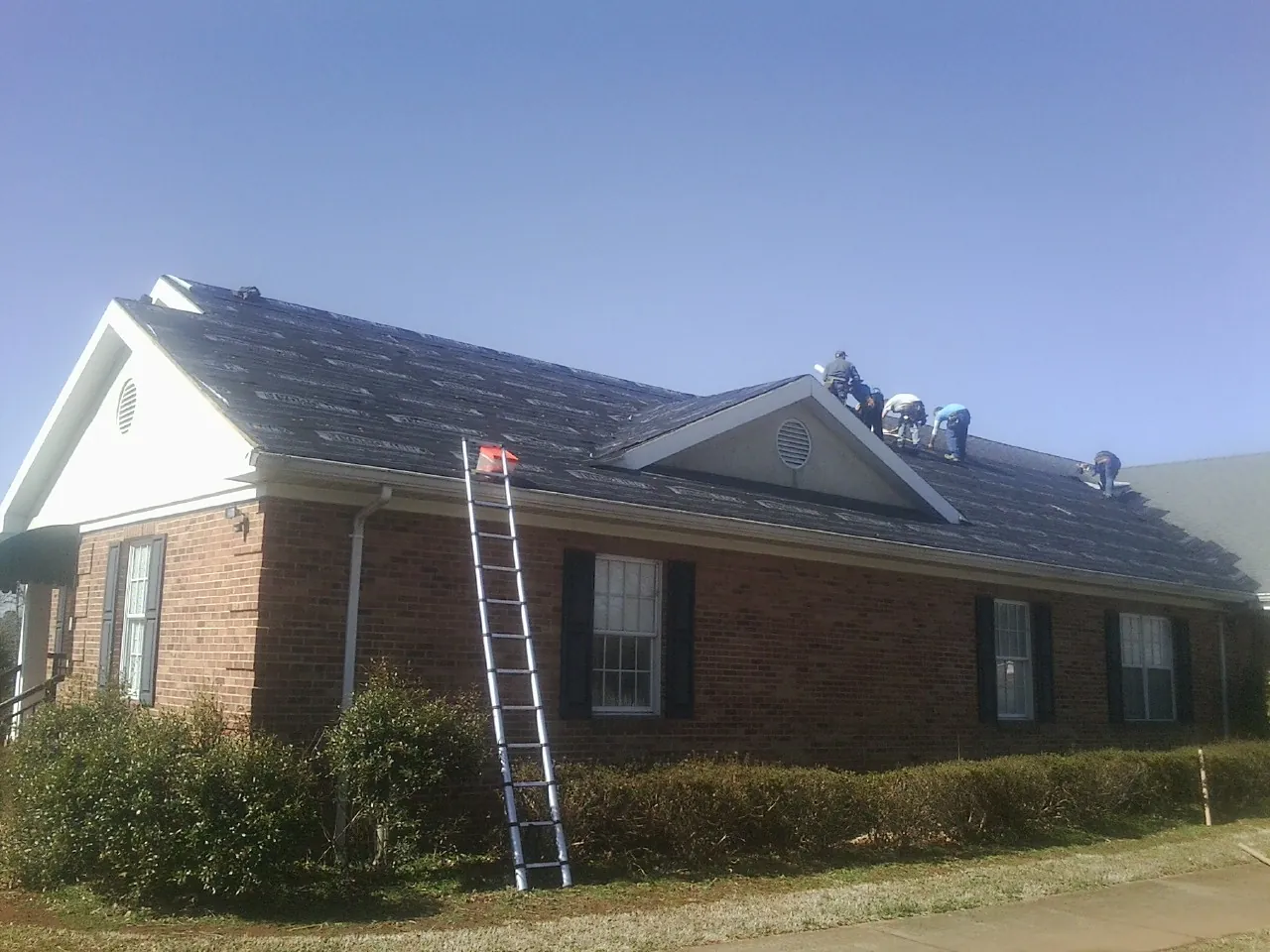 Crew tearing shingles off a brick ranch roof with a ladder set — Emergency Roof Repair work by our crew in Nicollet