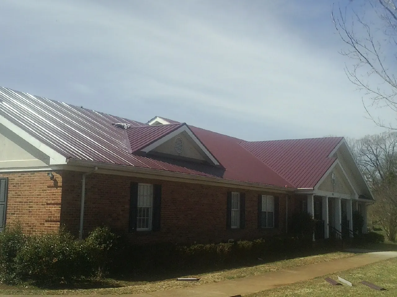 Red metal roof with gabled entries on a long brick building, from a Hail Damage Roof Repair job in Nicollet