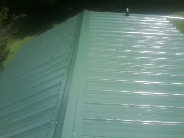New green metal panels meeting at the ridge of a roof — Flat Roof Repair work by our crew in Nicollet