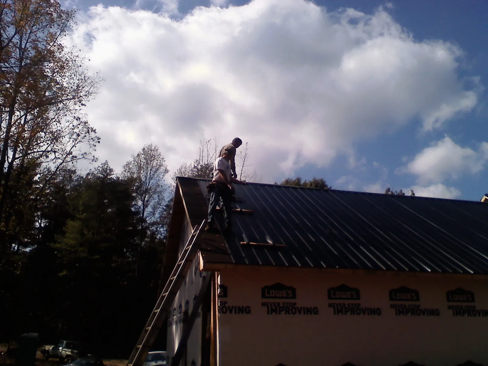Roofer fastening dark metal panels high against a cloudy sky, from a Roof Inspection job in Nicollet